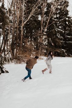 two people are playing in the snow near trees