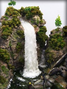 there is a large waterfall in the middle of some rocks and trees on top of it