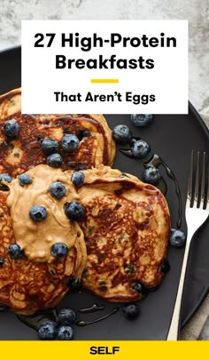 pancakes with blueberries and peanut butter are on a black plate next to a fork