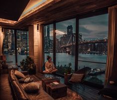 a woman sitting on a couch in front of a window overlooking the city at night