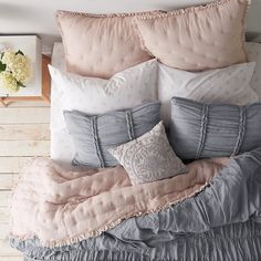 a bed with pink and grey pillows on top of it next to a white wall