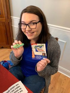 a woman sitting on the floor holding two toothbrushes and a package of dental floss