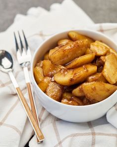 a white bowl filled with apple slices next to silverware