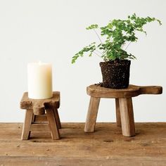 two small wooden stools with a potted plant on one and a lit candle on the other