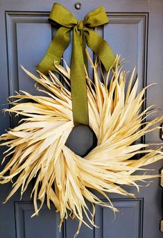 a wreath with a green bow hanging on the front door, decorated with dried corn stalks