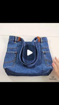 someone is holding a purse made out of blue jeans with an orange stitching on the bottom