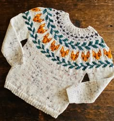 a sweater with an orange and blue design on it sitting on top of a wooden table