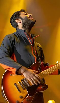 a man is singing and playing an electric guitar on stage with his eyes closed, while he's looking up to the sky