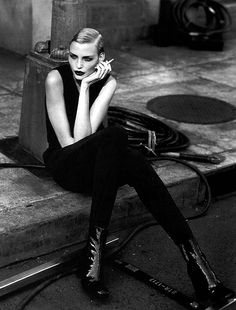 a black and white photo of a woman sitting on a ledge with her hand under her chin