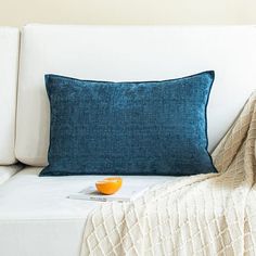 a blue pillow sitting on top of a white couch next to a blanket and an orange