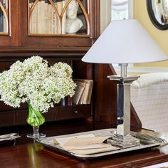 a table with a lamp and flowers on it in front of a bookcase filled with books