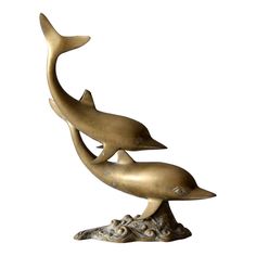 a bronze statue of two dolphins sitting on top of a tree stump in front of a white background