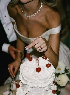 the bride and groom are cutting their wedding cake with cherries on each tiers