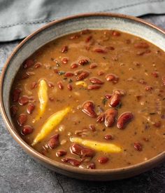 a brown bowl filled with beans and other food on top of a gray table cloth