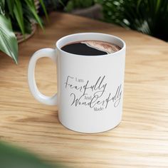 a white coffee mug sitting on top of a wooden table next to a green plant