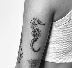 a black and white photo of a woman's arm with a seahorse tattoo on it