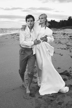 a man and woman standing on top of a beach next to the ocean with their arms around each other