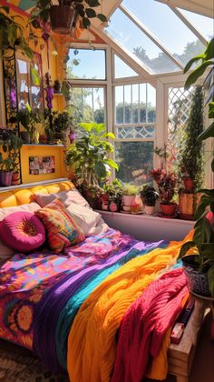 a bed with colorful blankets and pillows in a room filled with potted plants on the windowsill