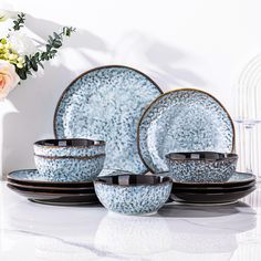 a set of blue and black dishes with flowers in the background on a white table