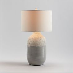 a gray and white table lamp with a beige shade on the top, in front of a grey background