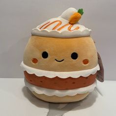 a stuffed toy hamburger with a carrot on top and whipped cream on top, sitting on a white surface