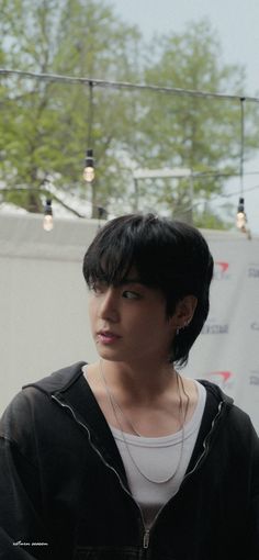 a young man with black hair wearing a white t - shirt and silver earrings