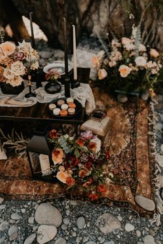 a table topped with candles and flowers on top of a rug next to rocks covered in dirt