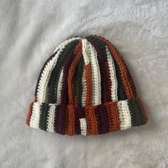 a multicolored knitted hat laying on top of a white bed coverlet