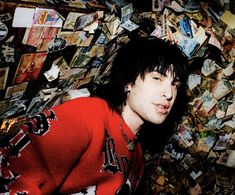 a man with black hair and red sweater standing in front of a pile of money