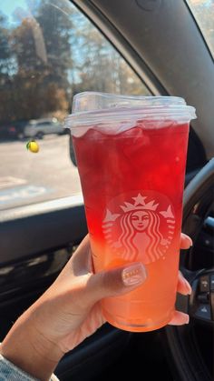 a person holding up a drink in their hand while sitting in the driver's seat of a car