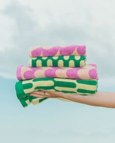 a person's hand holding three towels in front of blue sky with clouds behind them