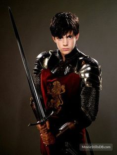 a young man dressed in medieval armor holding two swords and posing for the camera with his hands on his hips