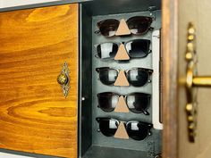 an open wooden case with many pairs of sunglasses in it's display compartment on the wall