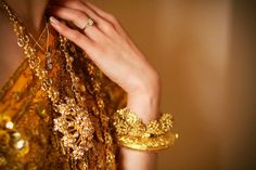 a close up of a person's hand with gold jewelry on their arm and dress