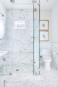 a bathroom with marble walls and flooring, including a glass enclosed shower stall next to a white toilet