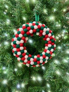 a christmas ornament hanging from the top of a green and red wreath on a tree