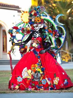 a woman in a red dress with flowers on her head and arms is dressed up like a skeleton