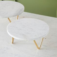 two white marble tables sitting on top of a counter next to each other with gold legs