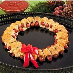 a wreath made out of pigs in a blanket on top of a black plate with red ribbon