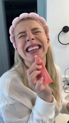 a woman is smiling and holding a piece of food in front of her face while wearing a pink hat