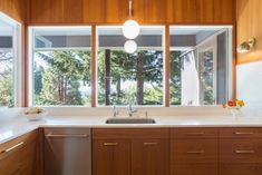 a kitchen with wooden cabinets and white counter tops, along with a large window overlooking the trees