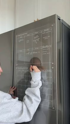 a woman is writing on the side of a refrigerator