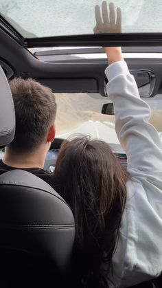 a man and woman sitting in the back seat of a car with their hands up