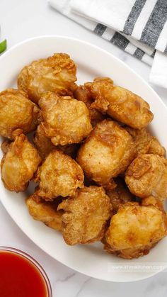 some fried food on a white plate next to ketchup and dipping sauces