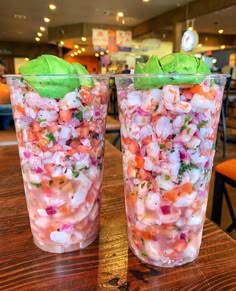 two plastic cups filled with food sitting on top of a wooden table next to each other