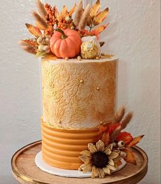 a three tiered cake decorated with fall leaves and pumpkins on a wooden stand