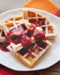 waffles on a white plate topped with syrup and fruit topping, sitting on a table