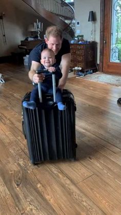 a man holding a baby sitting on top of a suitcase