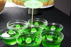 green jello cups are arranged on a table with a cake and cupcakes in the background