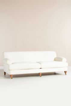 a white couch sitting on top of a white floor next to a wall and wooden legs